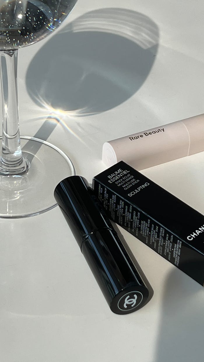 Elegant flat lay of beauty products and a wine glass on a white surface with natural lighting.