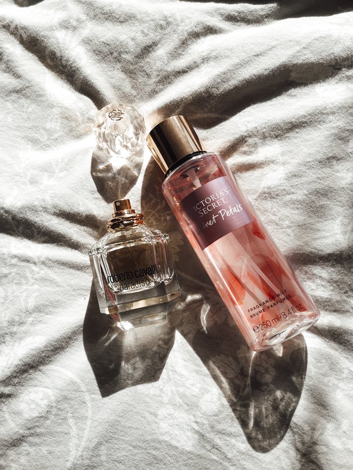 A pair of sunlit perfume and fragrance bottles on a soft white surface, creating a serene and luxurious feel.