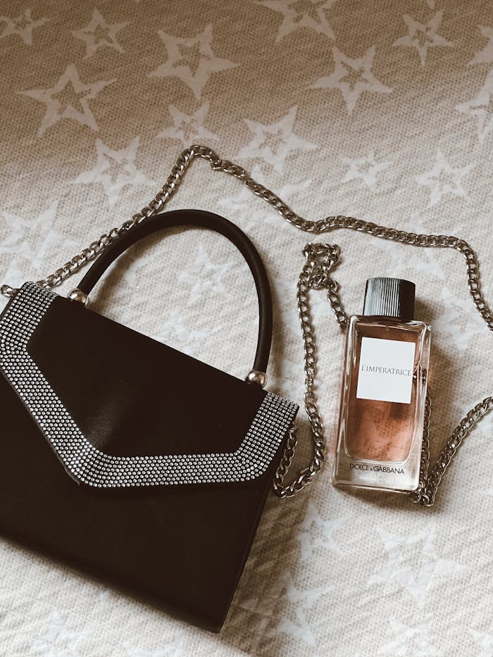 Elegant handbag with chain strap and Dolce & Gabbana perfume on a star-patterned fabric.