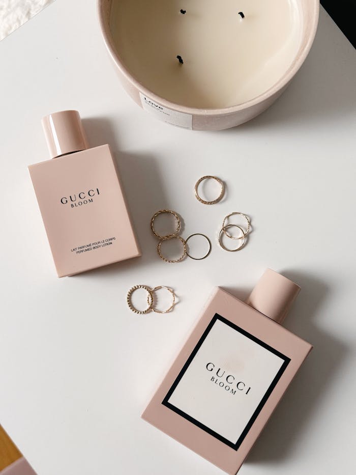 Stylish flat lay featuring Gucci Bloom perfume bottles, gold rings, and a candle.